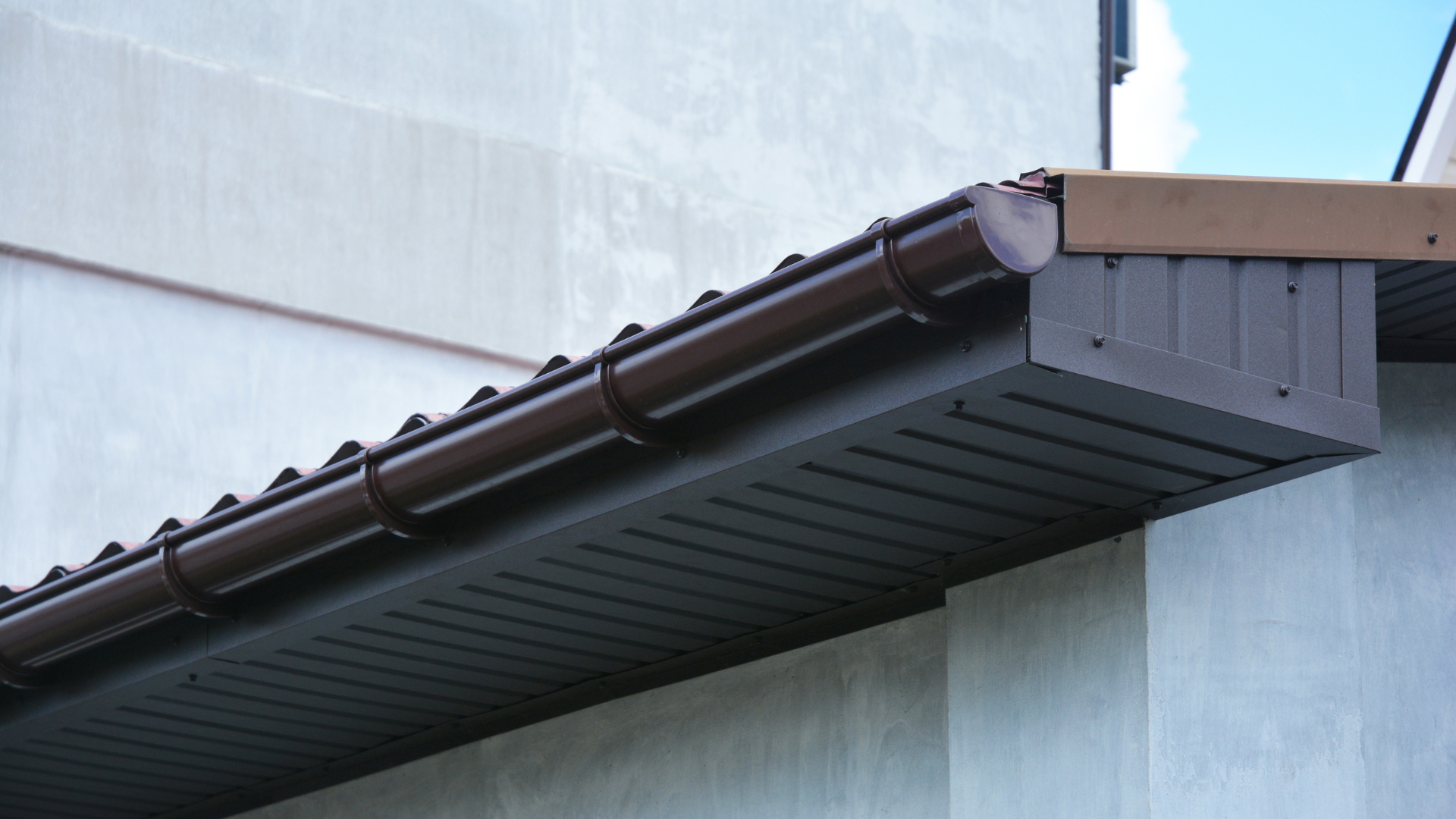 New dark fascia board, vented soffit and guttering fitted along the eaves of a tiled roof